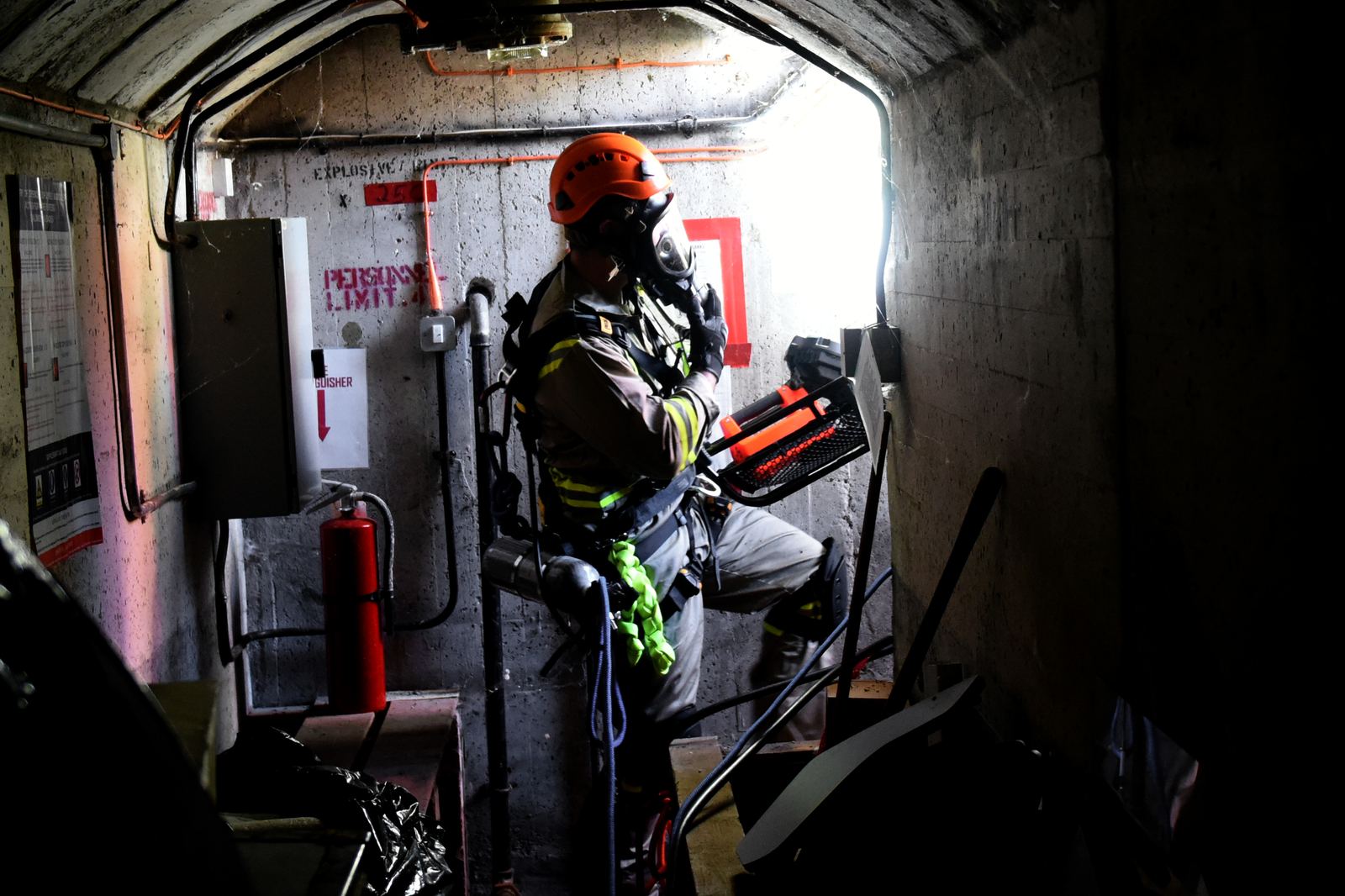 Worker in a hard hat, harness and breathing apparatus inside a tight concrete confined space