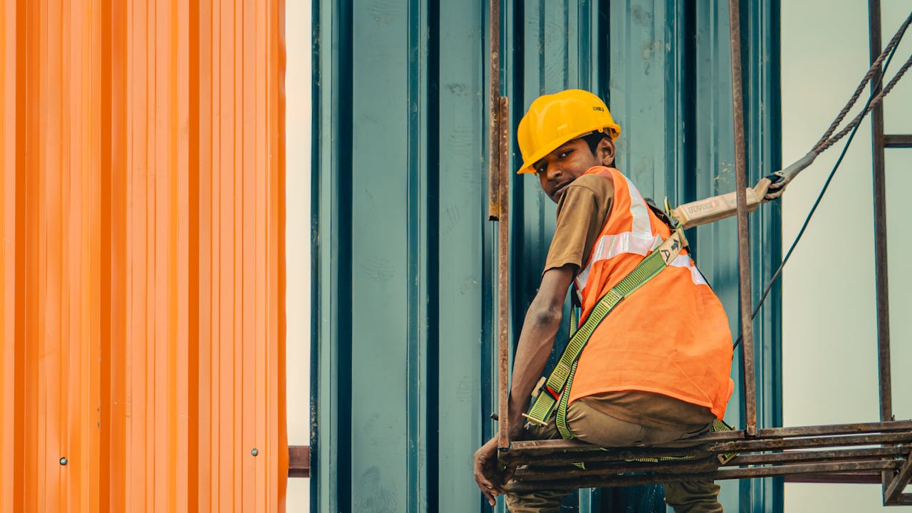 Construction worker at height in a hard hat and fall-arrest harness on scaffolding