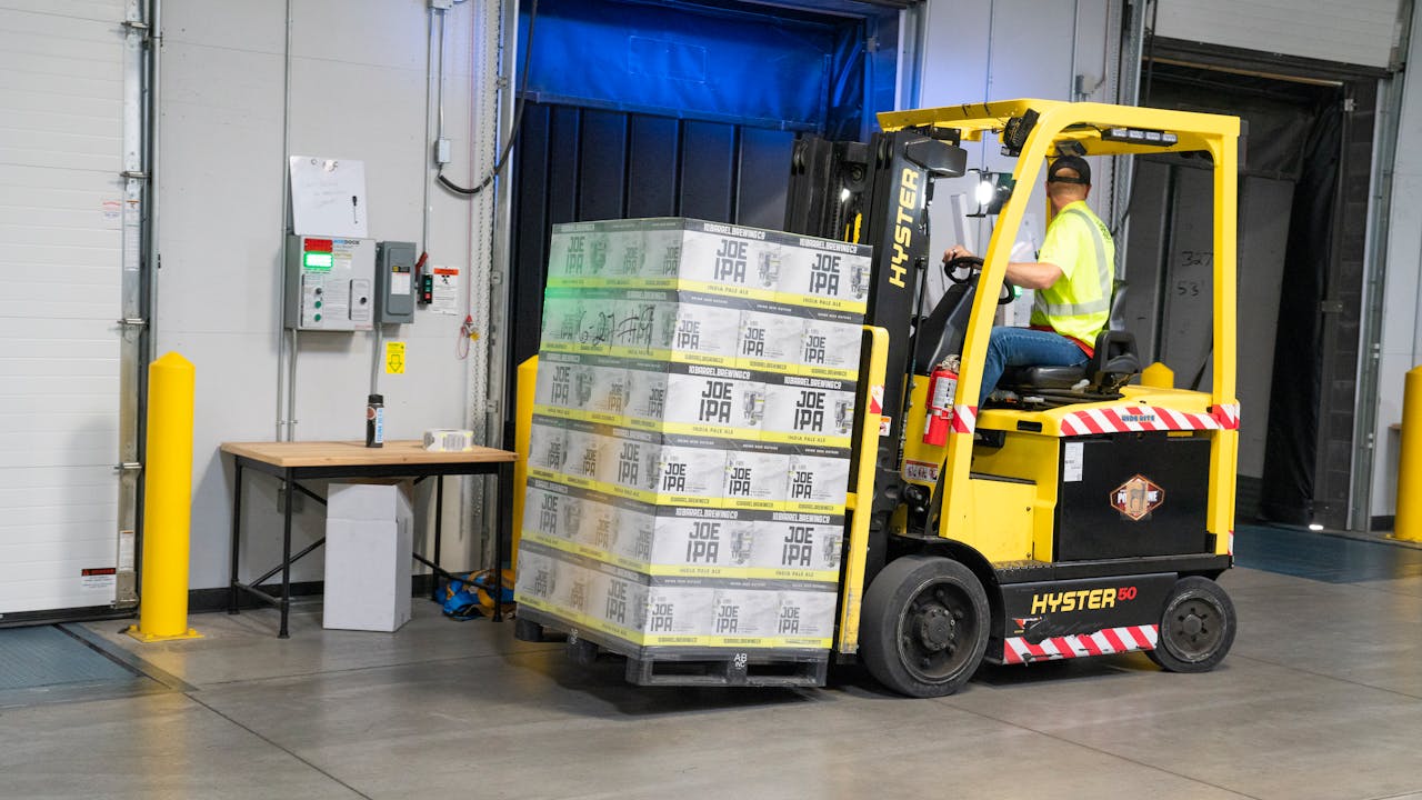 Forklift operator in a high-visibility vest moving a pallet at a warehouse loading dock