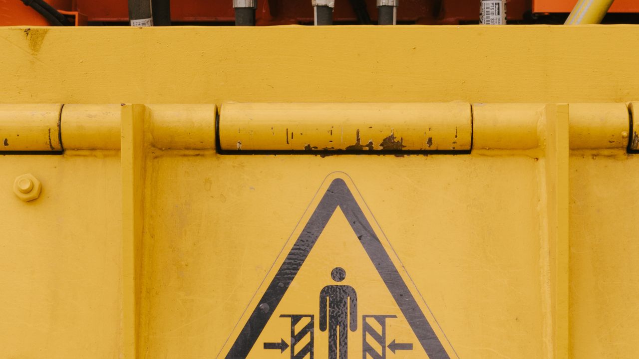 Yellow industrial machine with a crush-hazard warning sign marking a danger zone